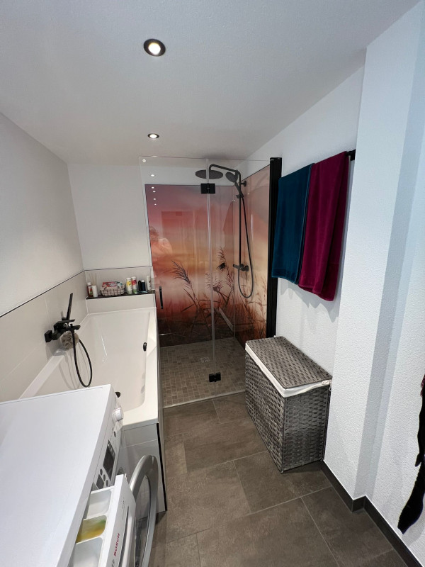 Dusche mit Fotorückwand und Badewanne im schmalem Bad.